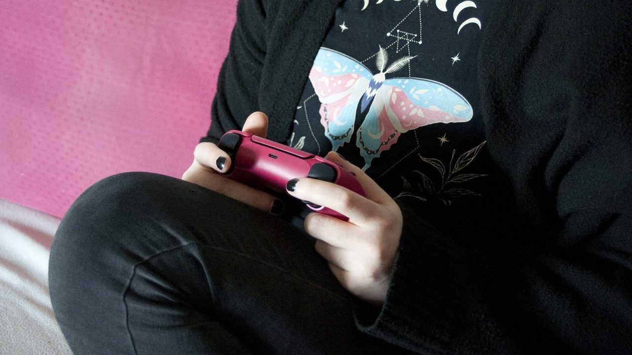 Person on a sofa holding a red DualSense controller while playing
