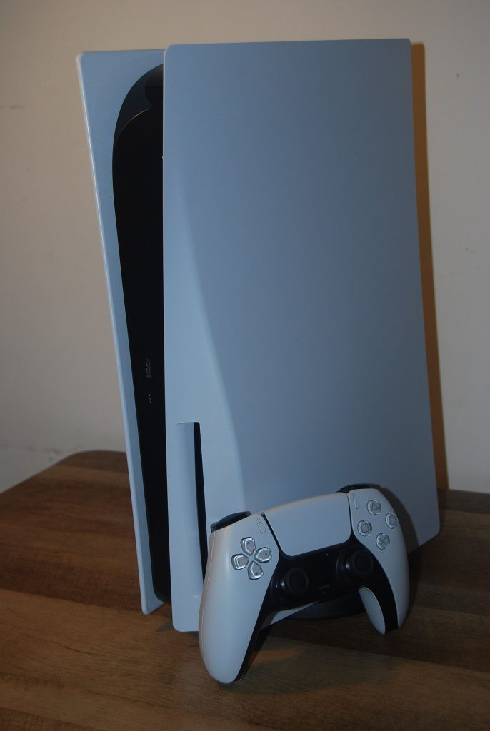 Standard PS5 standing upright on a wooden shelf with a DualSense