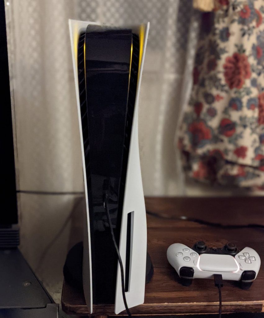 Original launch-design PS5 standing upright next to a white DualSense controller