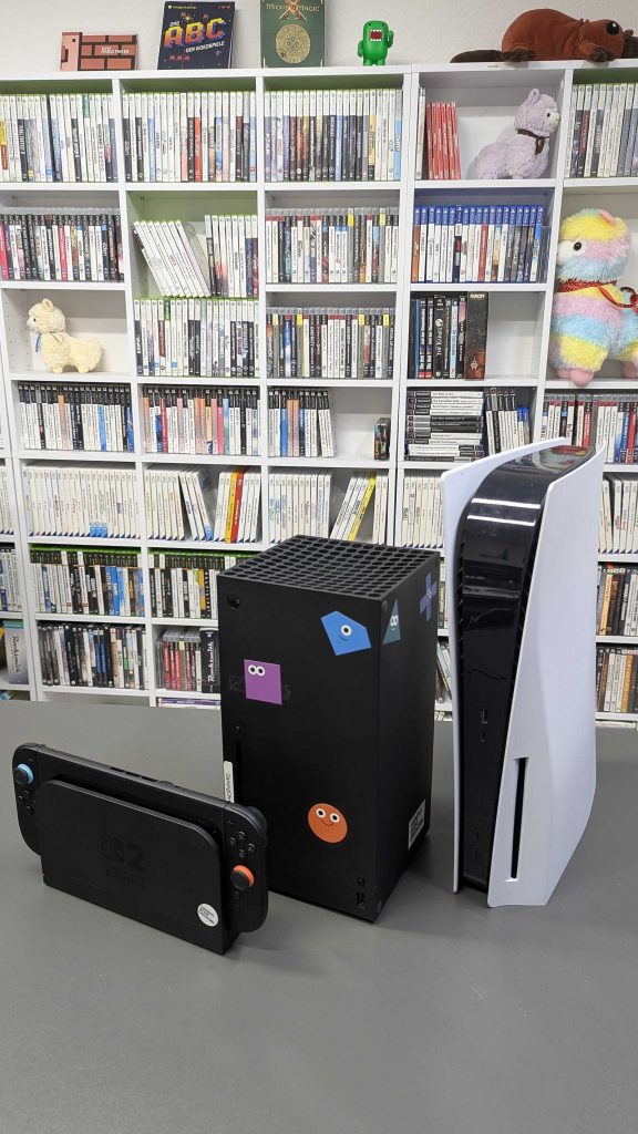 Xbox Series X, PS5 and Xbox Series S standing together in front of a bookshelf